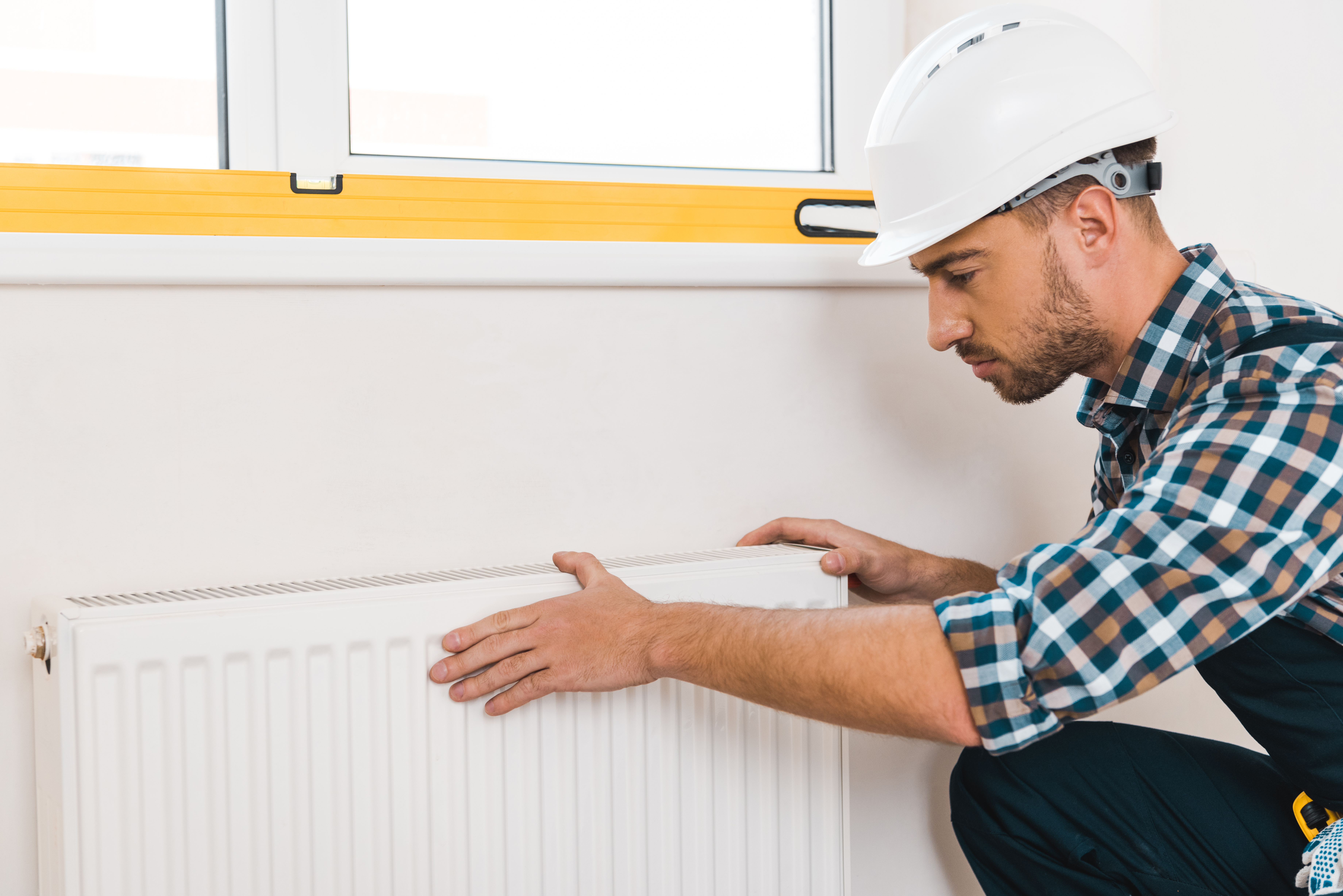 handsome handyman in helmet sitting near heating radiator